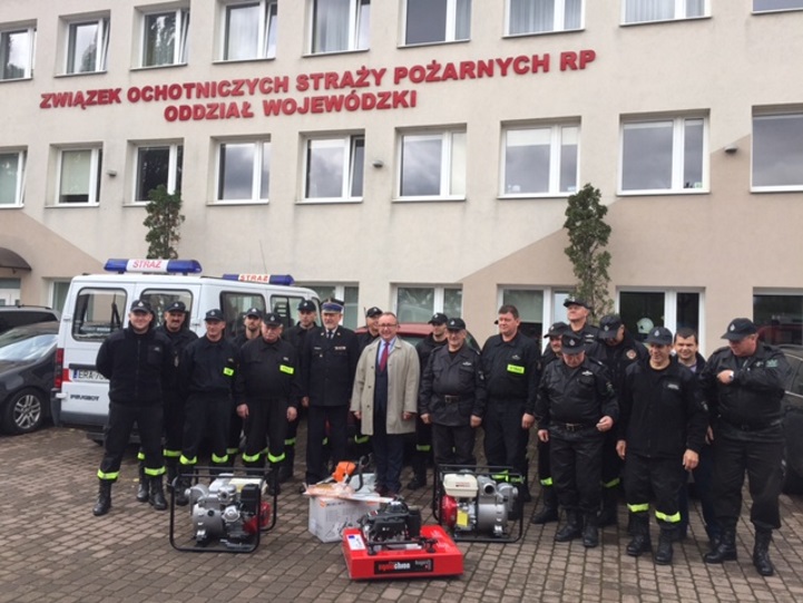 Prezes WFOŚiGW w Gdańsku Maciej Kazienko wraz ze strażakami OSP województwa pomorskiego. Na ziemi leży  specjalistyczny sprzęt dla strażaków.